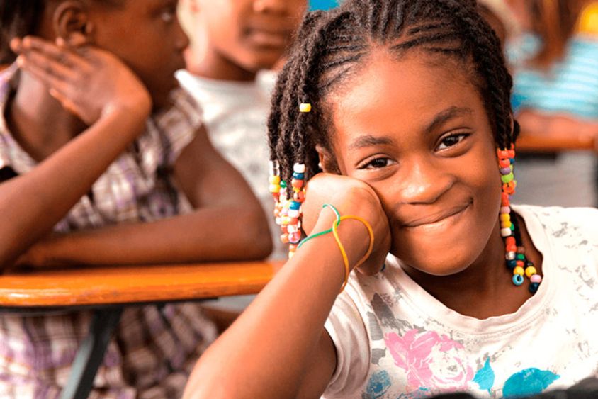 A girl smiles sitting at a desk in the classroom - Inter-American Development Bank - IDB